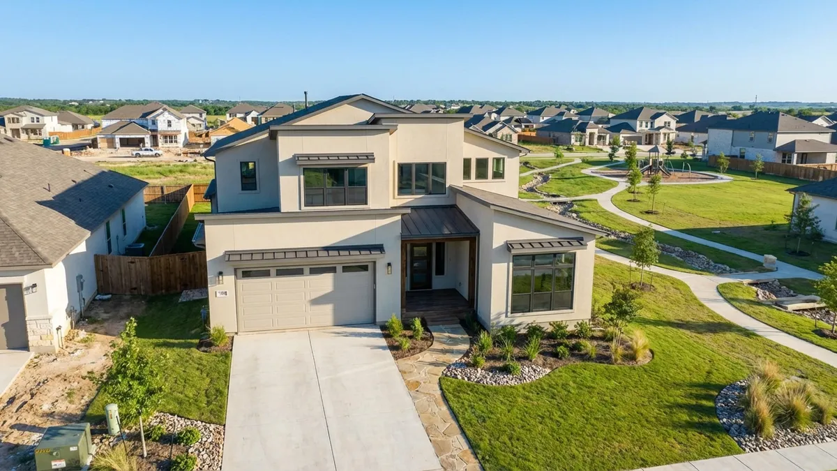 High-angle drone shot of a modern, newly built single-family home in a Ponder, Texas new construction community, showcasing a manicured front lawn, a two-car garage, and contemporary architectural elements. The house is light-colored stucco with dark trim, under a clear blue Texas sky. In the background, other new homes are visible, interspersed with green spaces and nascent community amenities like a small park area. Cinematic lighting, bright daytime, 16:9, highly detailed 8k.