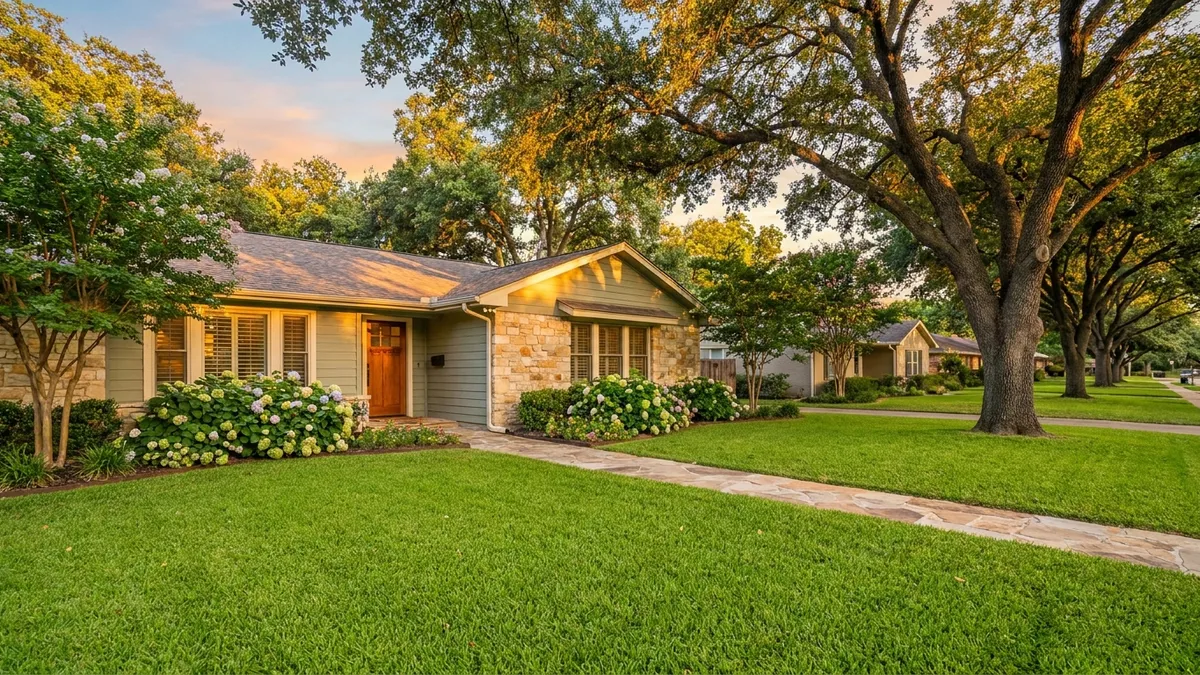 Close-up of a charming, well-maintained single-story ranch home in an East Bedford, TX neighborhood street with large, mature oak trees creating dappled sunlight. Cinematic lighting, golden hour, 16:9 aspect ratio, highly detailed 8k photography. Focus on the facade of the home, green lawn, blooming flower beds, and a glimpse of a tree-lined street extending into the background. Pastel tones with warm oranges and soft blues.