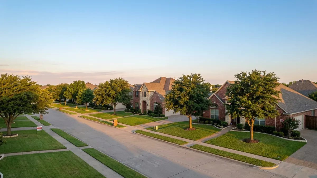 A wide-angle, aerial photograph capturing a quiet, tree-lined suburban street in Murphy, TX, bathed in soft morning light. The image features several well-maintained single-family homes with brick facades and manicured lawns. A 'for sale' sign is visible in front of one house, slightly in the distance. The sky is a clear, pastel blue. Cinematic lighting, golden hour, 16:9, highly detailed 8k.